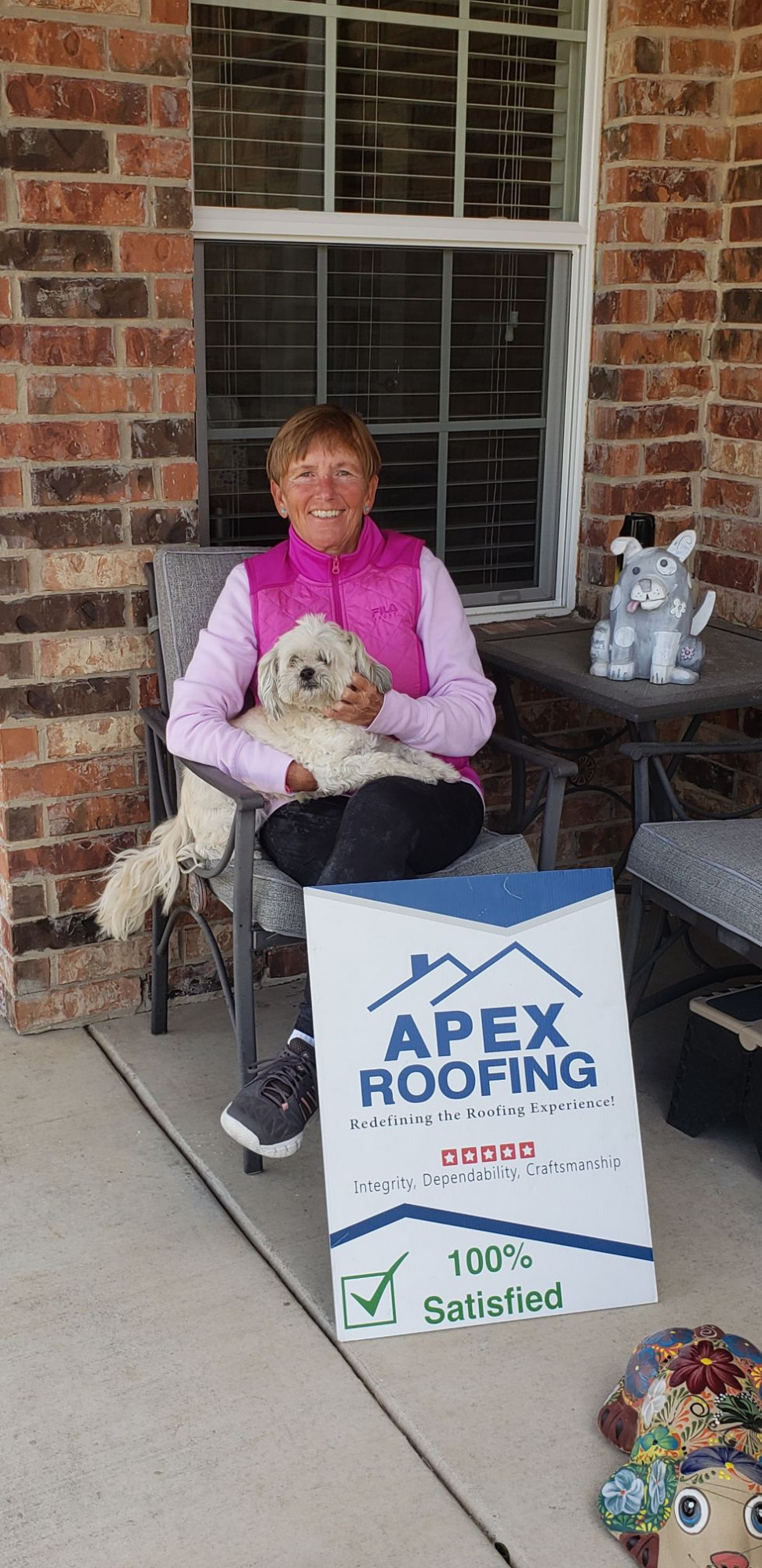 Woman holding her dog next to APEX Roofing Sign